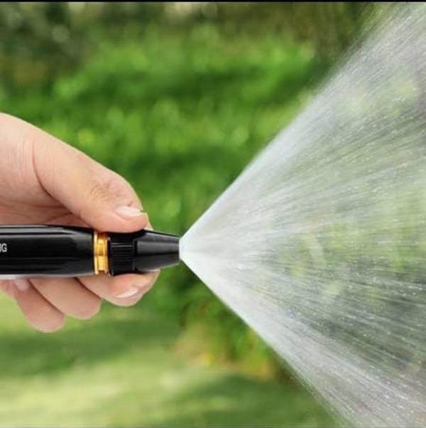 Hand holding a garden hose nozzle spraying water
